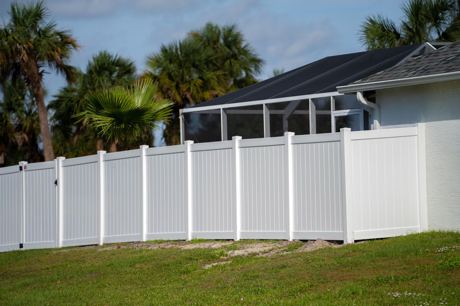 Green lawn enclosed by a white vinyl picket fence, roofline behind.