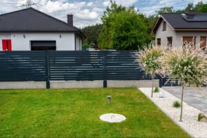 Houses with modern anthracite panel fences, sliding garage gates, and metal wicket doors.