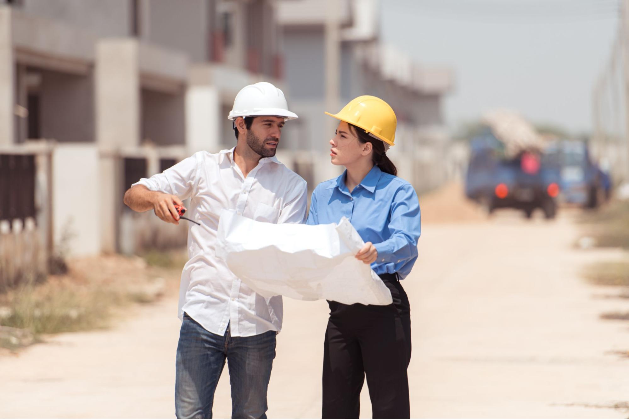 An architect and an engineer review a blueprint together while assessing progress at a residential home construction site.