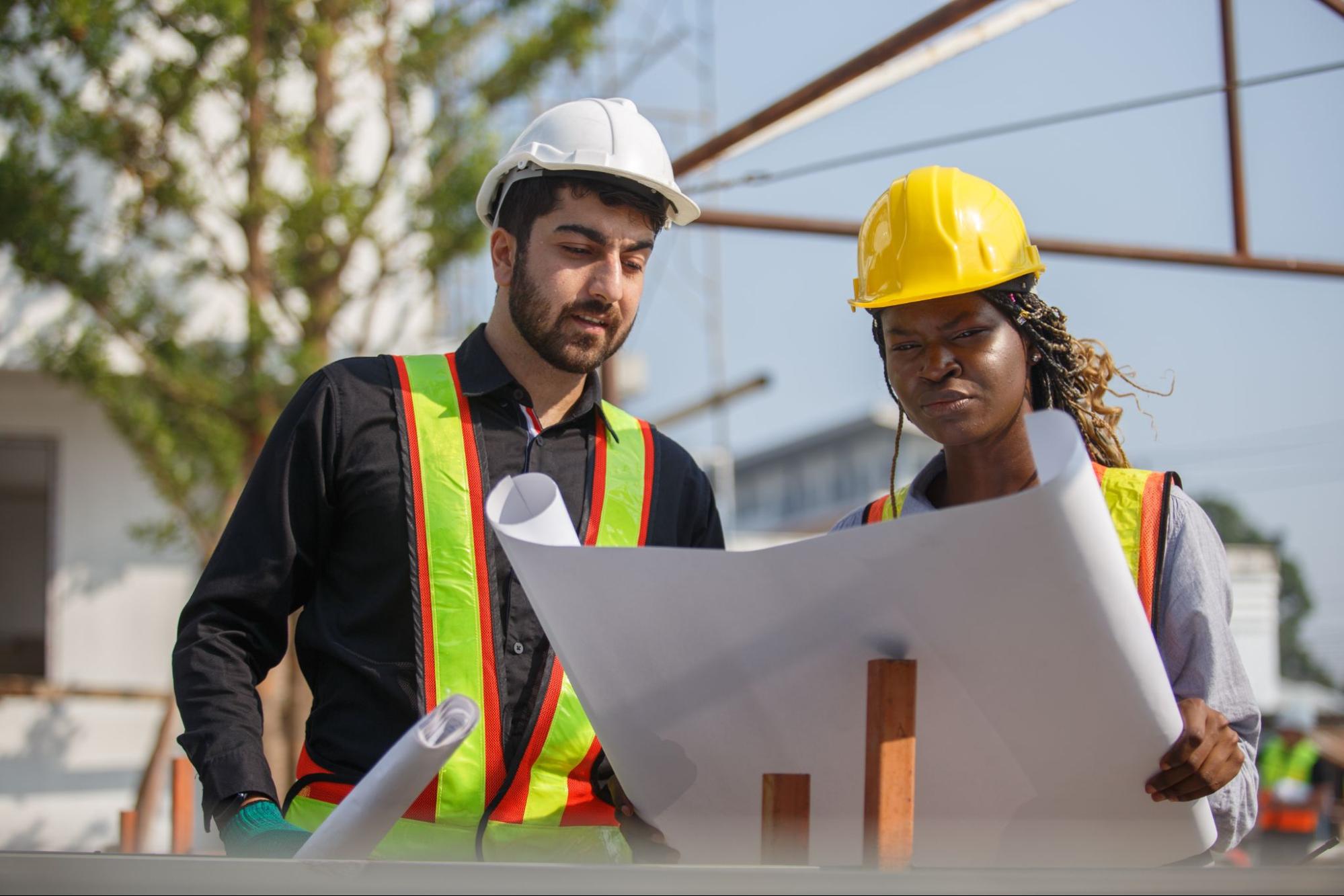 Construction contractors review detailed blueprints together at an active job site.