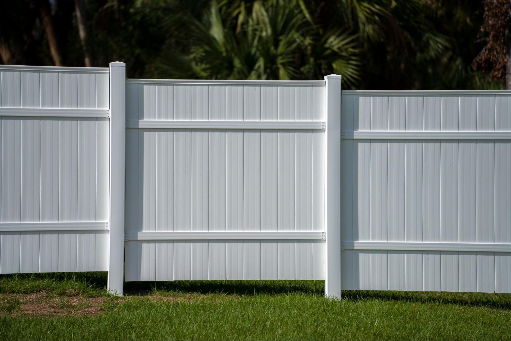 White vinyl picket fence enclosing lawn around residential property.