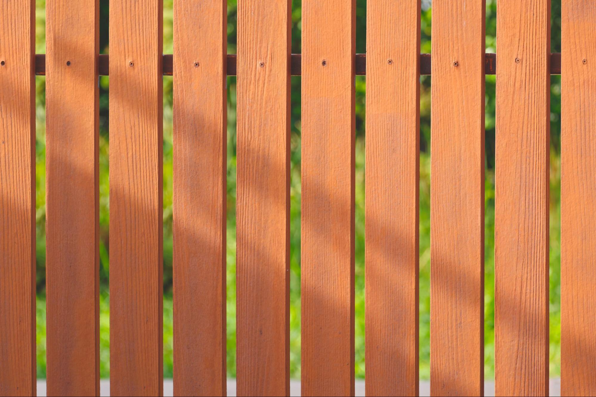 A close-up of a brown composite fence with sunlight and shadows.