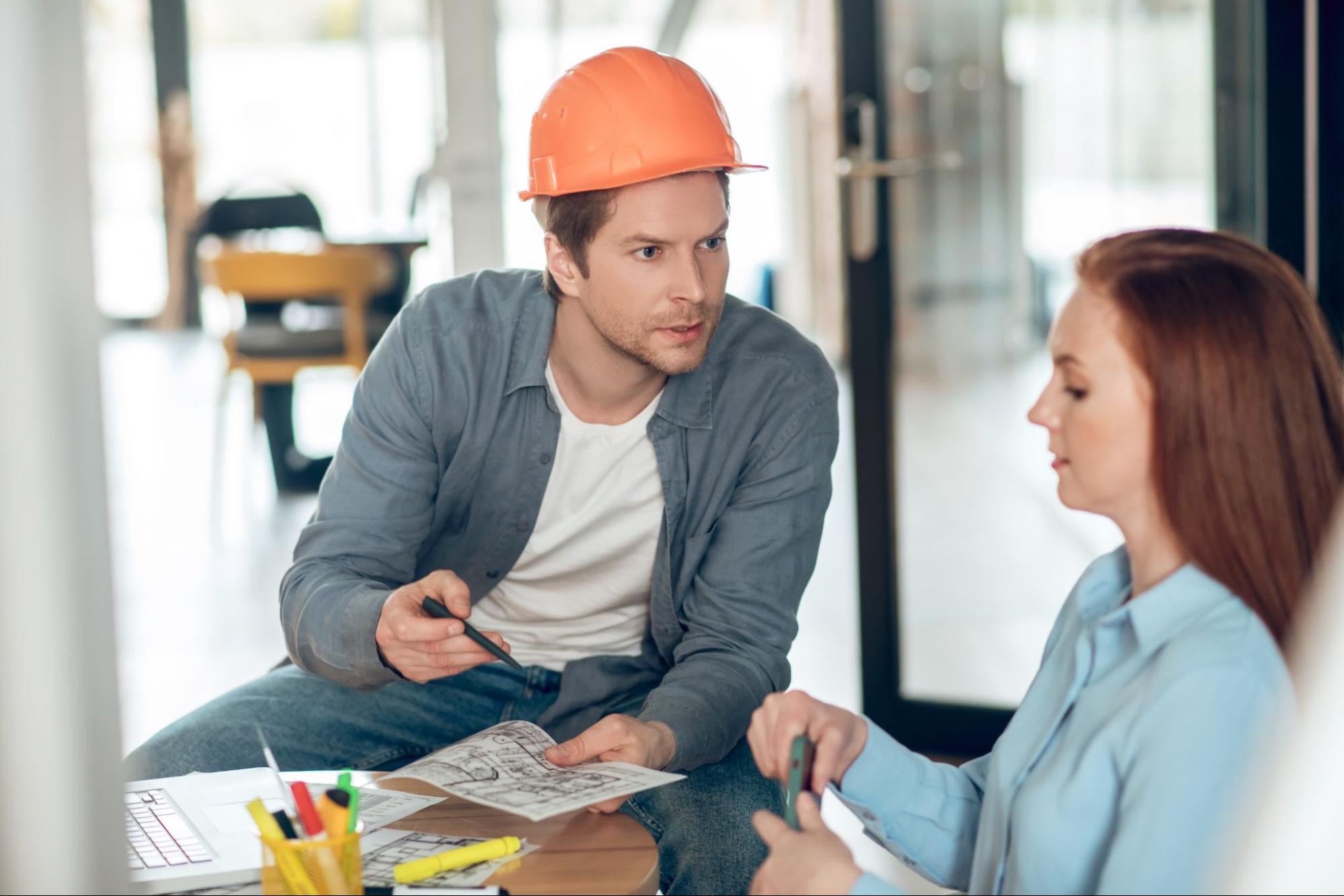 A construction contractor presents the building plans to a female client.