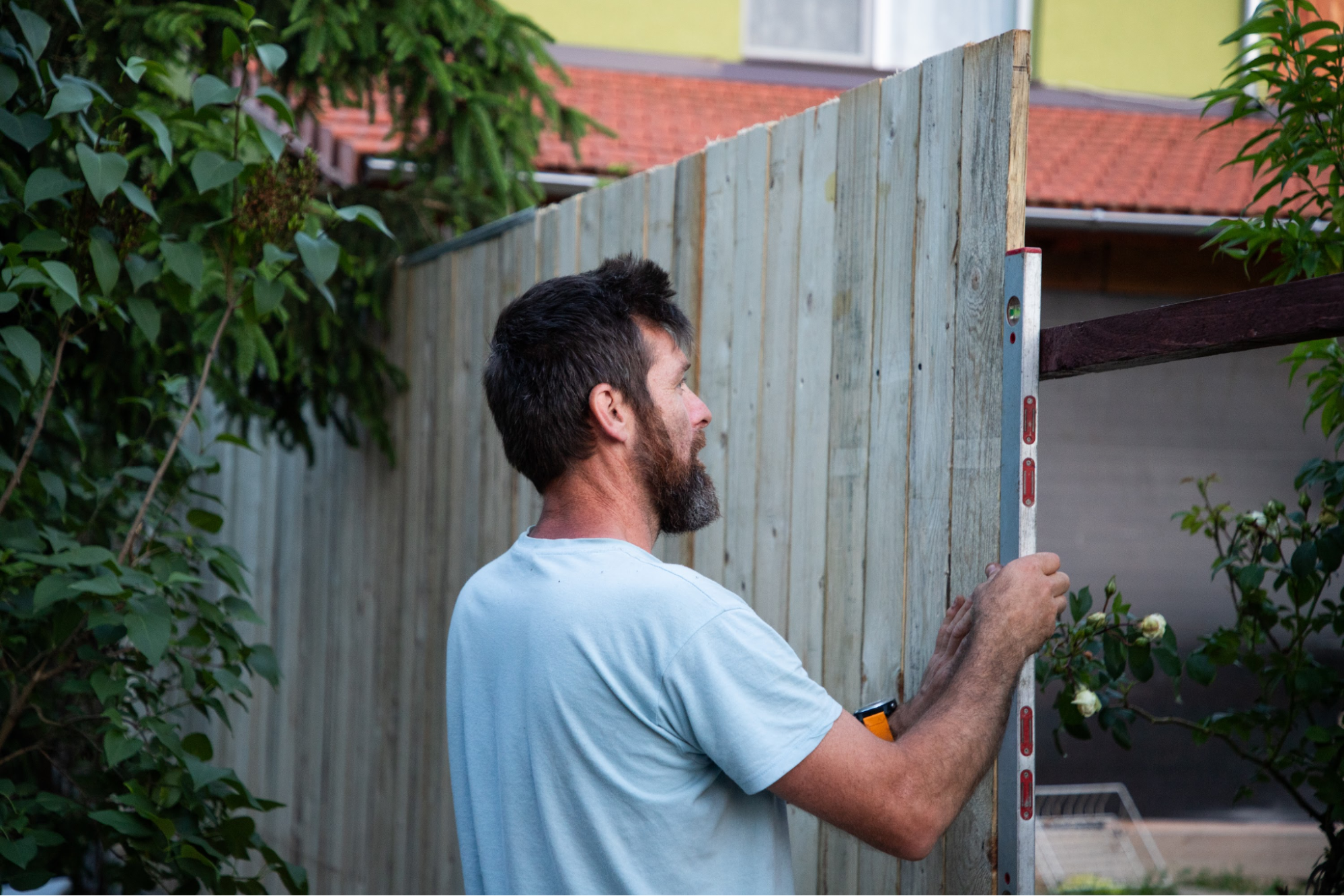 A man leveling a fence while installing it.